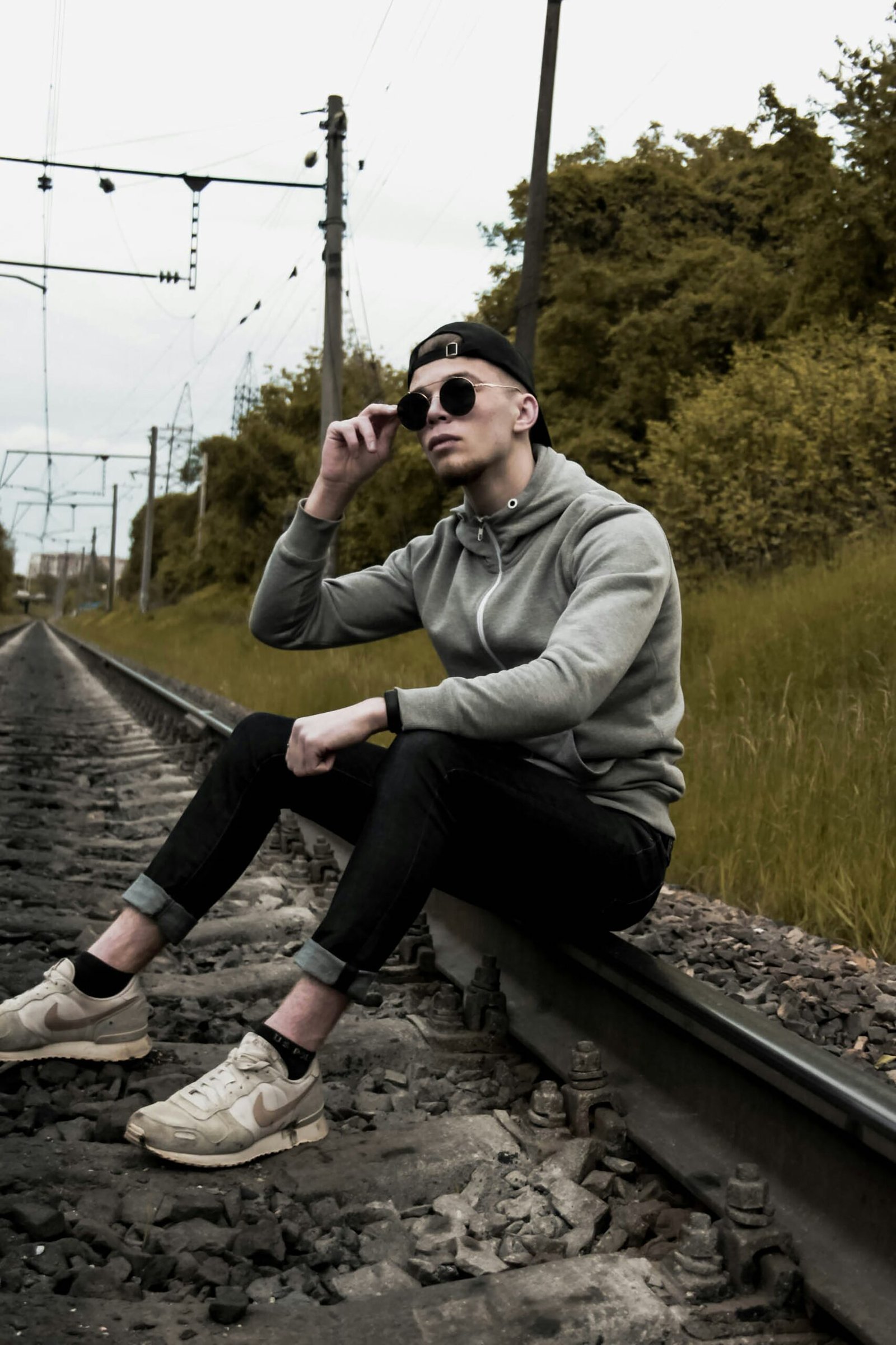 man in gray jacket and black pants sitting on train rail